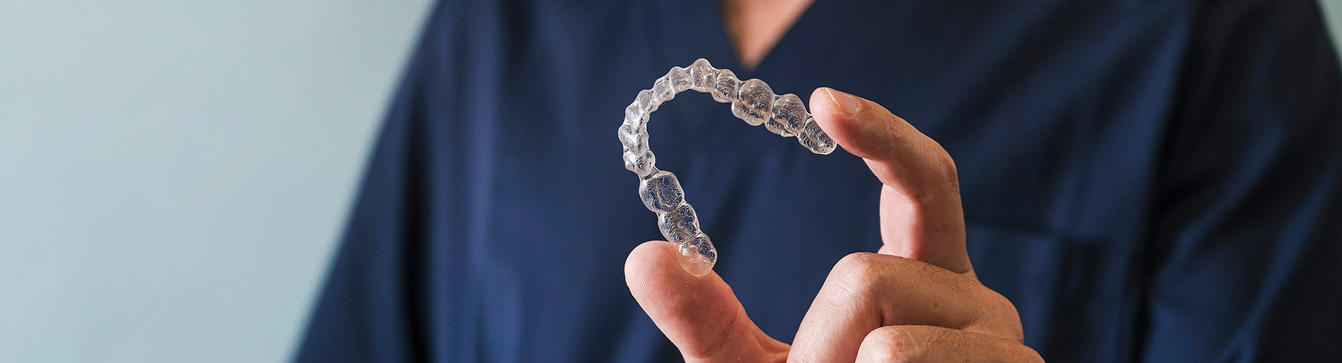A dentist is holding a Invisalign clear aligners.